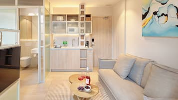 Ein modernes Wohnzimmer mit einer Couch, einem Couchtisch mit Flasche und Gläsern sowie einer Küchenzeile mit Mikrowelle und Schränken.