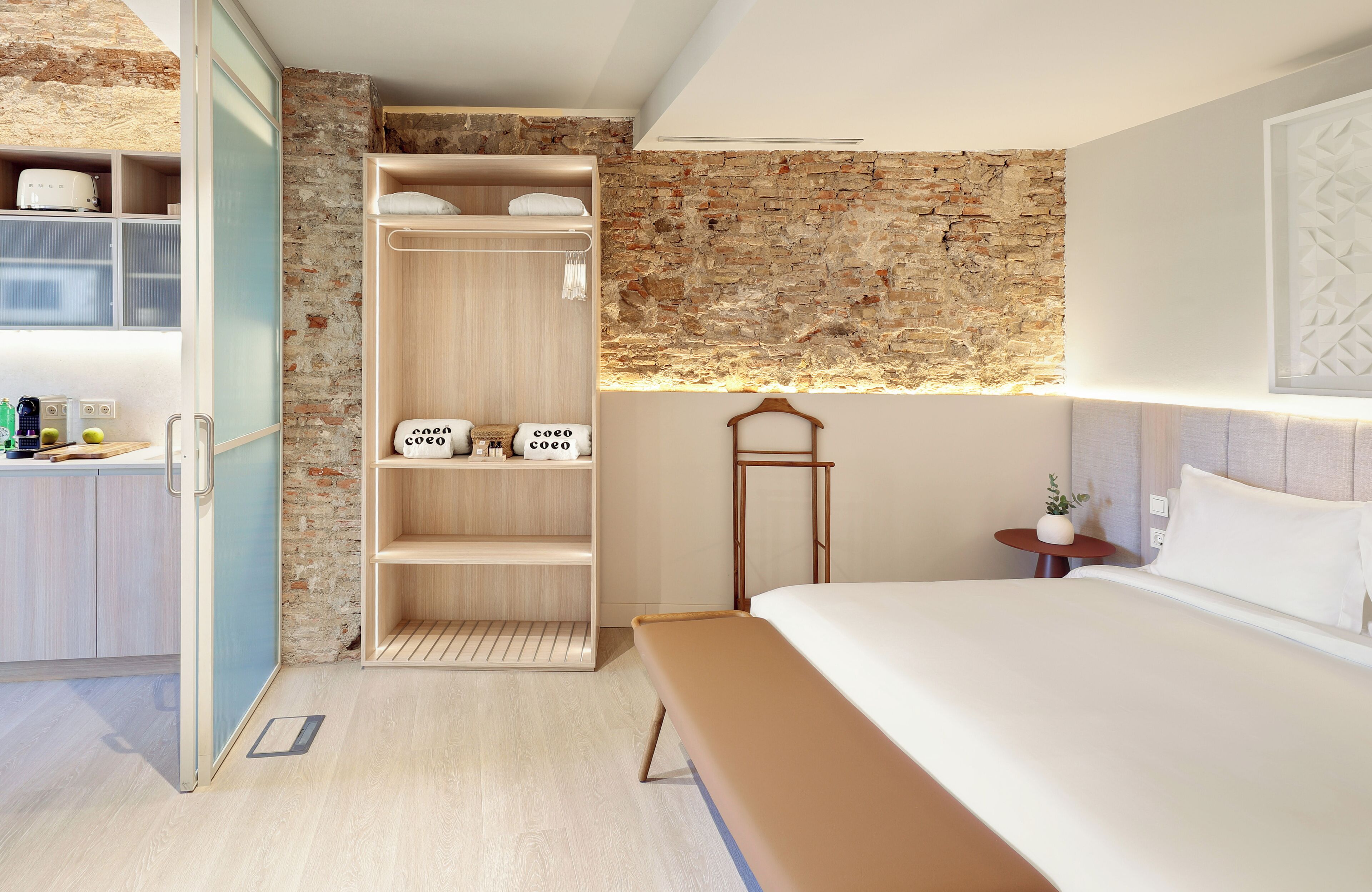 Ein modernes Hotelzimmer mit einem Holzschrank, einem Bett, einem kleinen Tisch mit einer Pflanze und einer Backsteinwand.