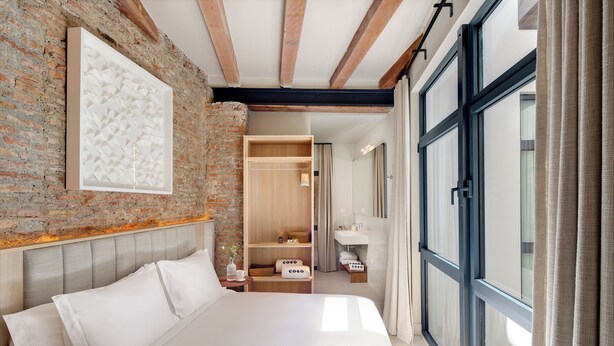 Een moderne slaapkamer met een bakstenen muur, een groot bed, een houten garderobe en een zichtbare badkamer door een open deur.