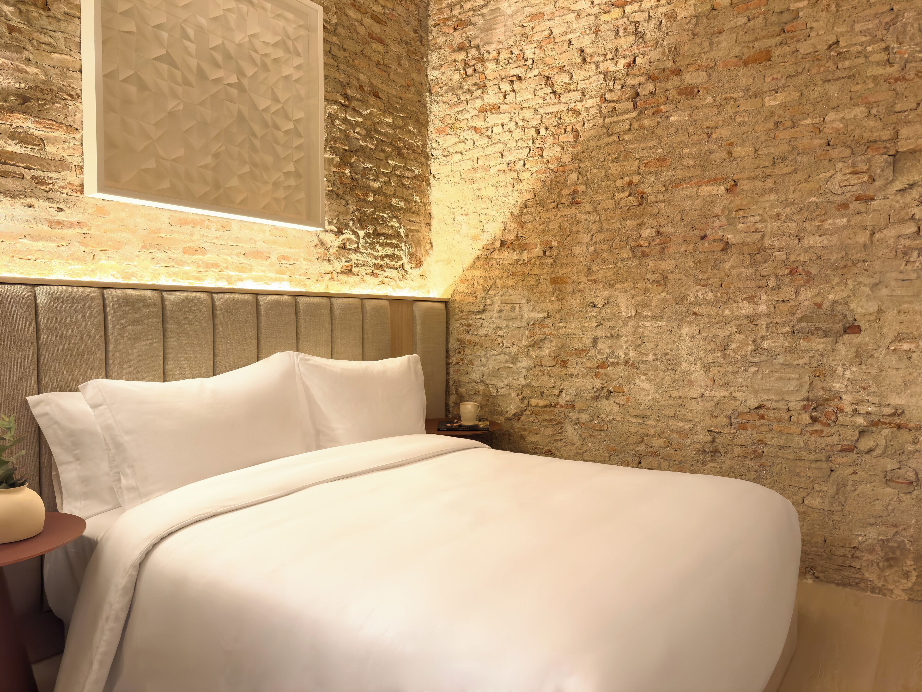 A bed in a room with a brick wall and a textured panel above it.