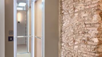 A hallway with a modern elevator, a brick wall, and a door leading to a room.