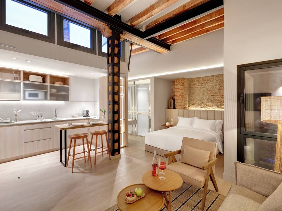 Une chambre d’hôtel moderne dotée d’un grand lit, d’un coin repas avec cuisine et offrant une vue sur la ville.
