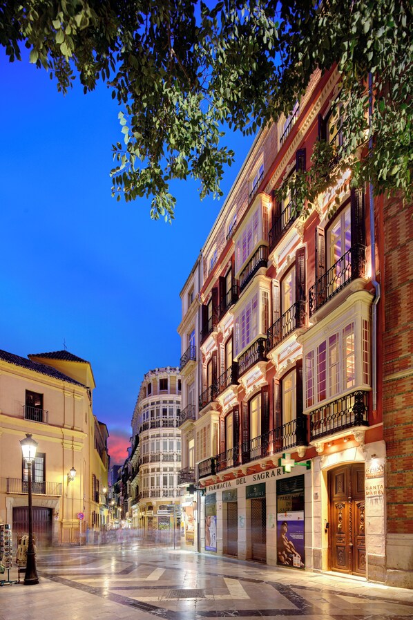 A historic street with ornate buildings, a pharmacy, and a well-lit plaza. - Coeo Santa Maria Signature Apartments  (Málaga)