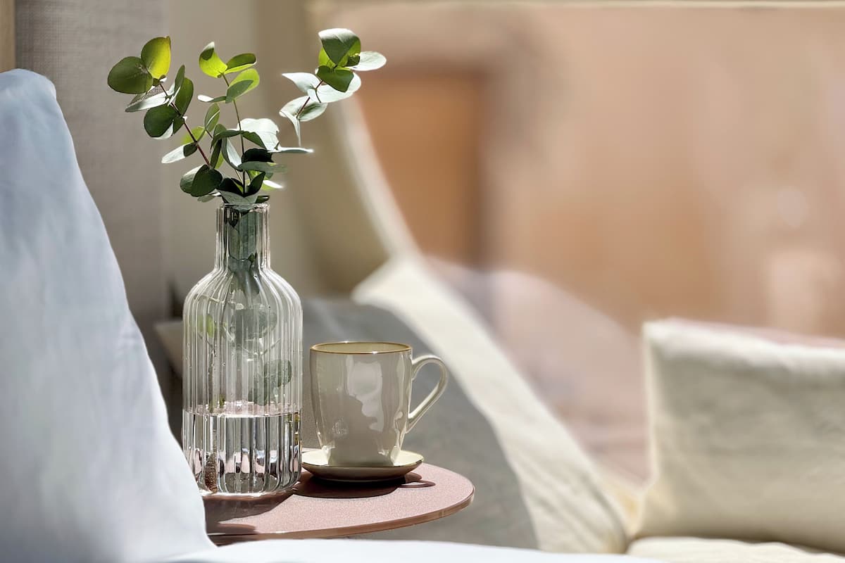 A clear glass vase with green leaves on a round table next to a white mug.