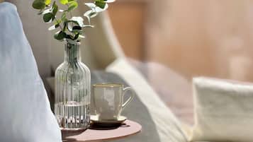 A clear glass vase with green leaves on a round table next to a white mug.