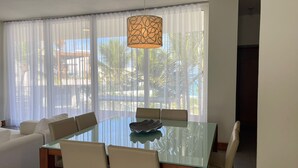 Een moderne eethoek met een glazen tafel, witte stoelen en een decoratieve lamp.
