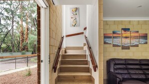 Eine Holztreppe mit Blick auf Bäume, ein an der Wand befestigtes abstraktes Gemälde und ein Ledersofa.