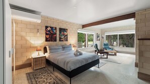Ein Schlafzimmer mit einem großen Bett, einem Nachttisch, einer Lampe, einem Sessel und Blick ins Freie durch eine Schiebetür.