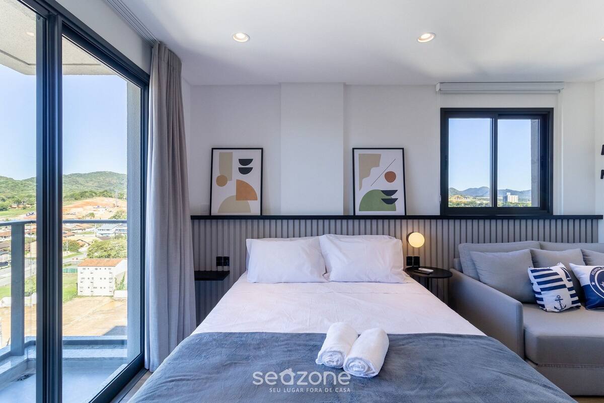Quarto de hotel com cama, sofá, janela ampla e obras de arte nas paredes.