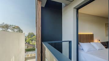 A hotel room with a balcony, a bed with white bedding, and a view of the outside.