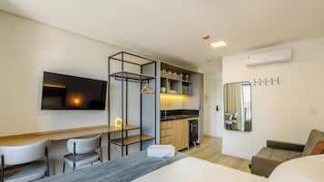 A modern hotel room with a bed, a desk, a chair, a kitchenette, and a bathroom.