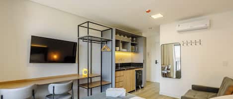 Ett modernt hotellrum med en säng, ett skrivbord, en stol, ett litet kök och ett badrum.