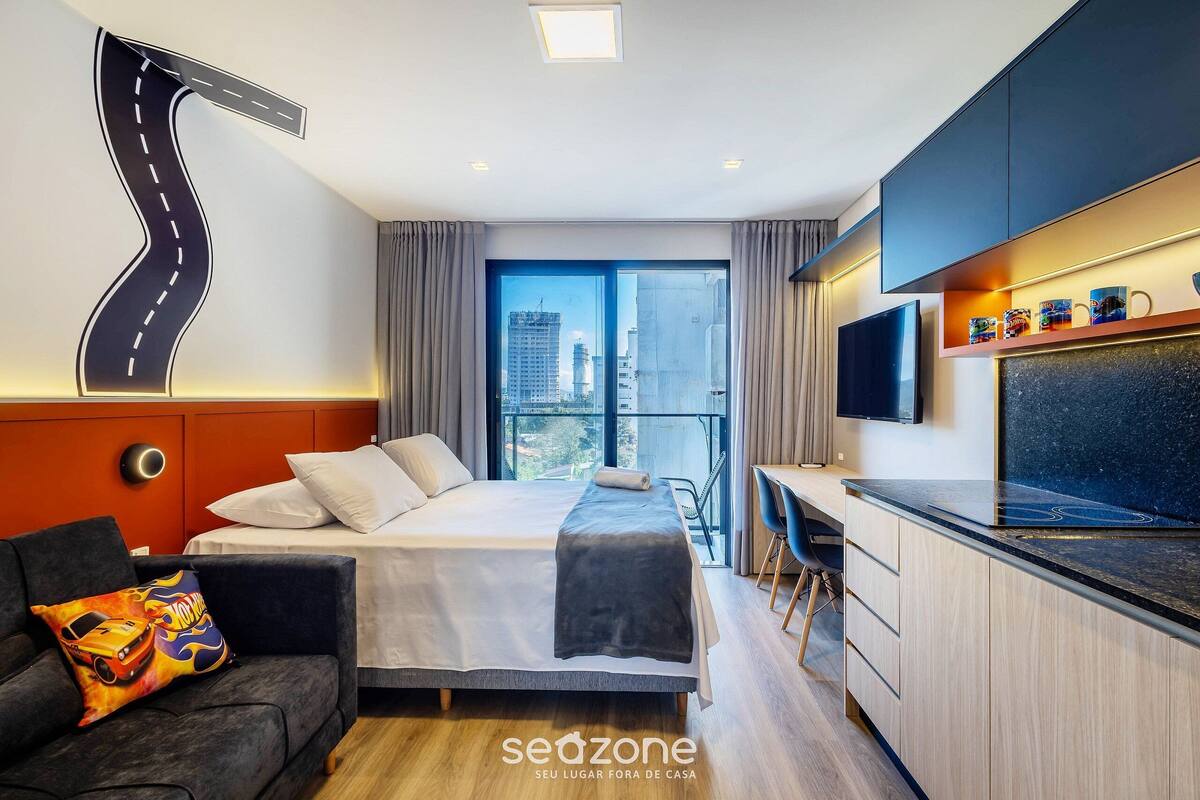 Quarto de hotel moderno com cama, sofá, escrivaninha, televisão e vista para a cidade.