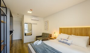 Una camera d'albergo con un letto, una sedia, una scrivania, uno specchio e un condizionatore d'aria a parete.