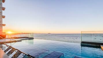 An infinity pool with a clear view of the sea and a sunset.