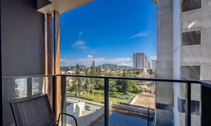 Un balcone con vista su un paesaggio urbano, che include edifici e una catena montuosa.