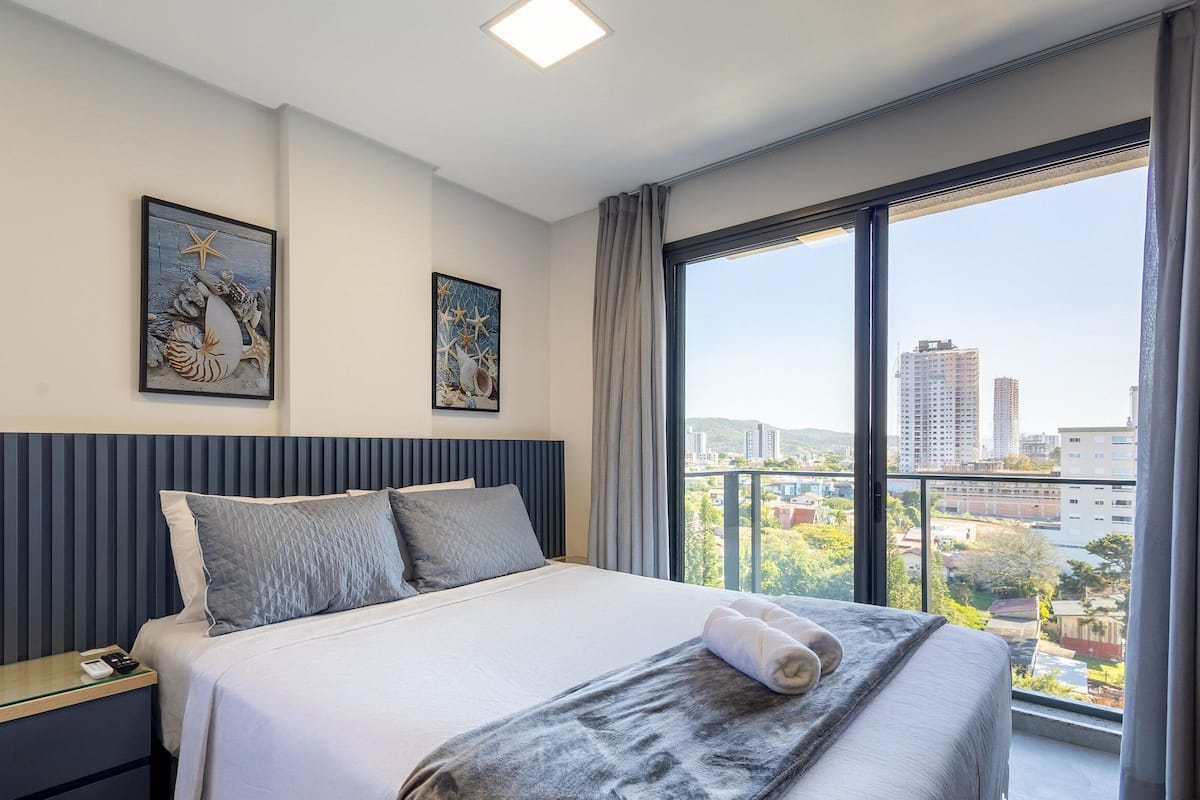 Quarto de hotel moderno com uma cama grande, uma mesa de cabeceira com telefone e duas obras de arte emolduradas na parede.