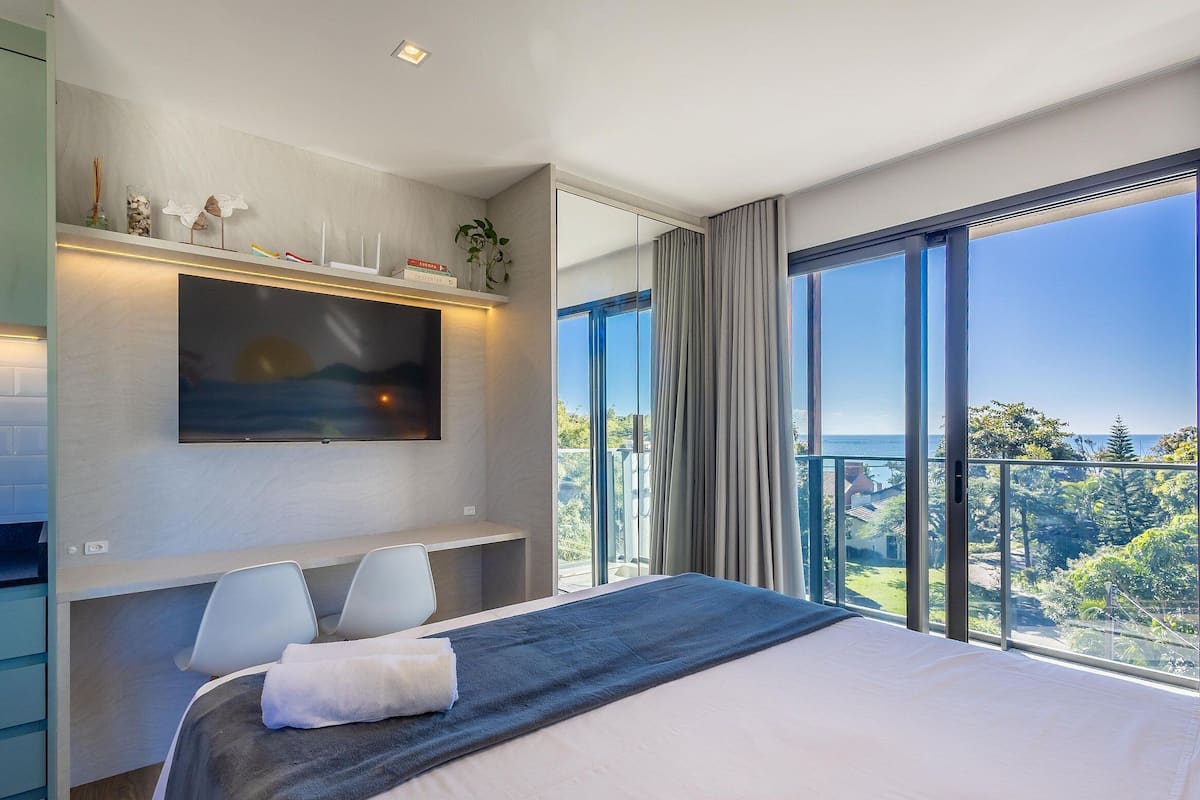 Quarto moderno com uma cama grande, televisão de tela plana na parede e varanda com vista para o mar.
