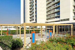 Edificio moderno con un espacio exterior cubierto que incluye equipo de ejercicio y un jardín con plantas en flor.