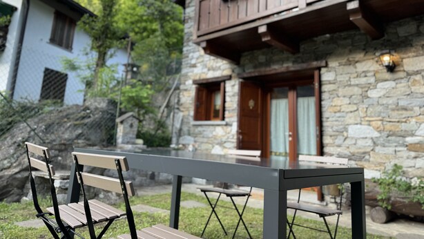 A stone building with a balcony, a wooden bench, and a table in a garden setting.