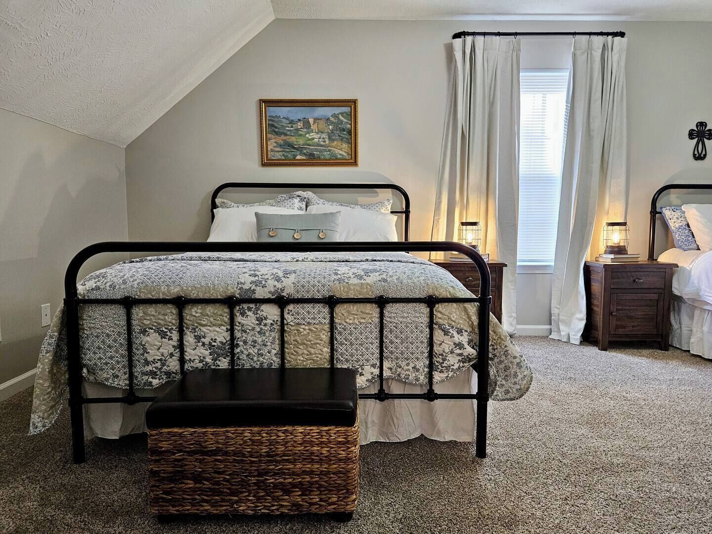 Een slaapkamer met een bed, nachtkastje, lamp, raam met gordijnen, en een schilderij aan de muur.