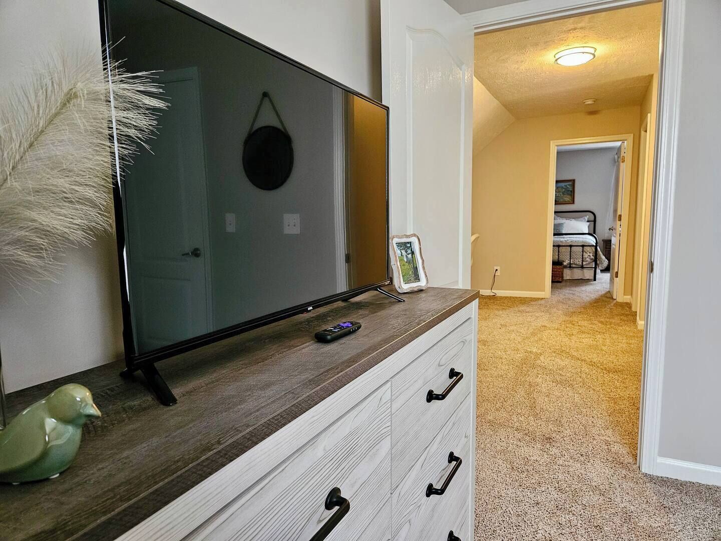 Un corridoio con una TV sopra un comò, un telecomando e un oggetto decorativo.