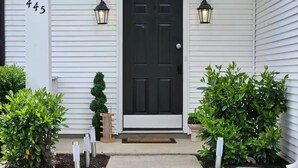 A front view of a house with a black front door, white siding, and two black wall-mounted lanterns.