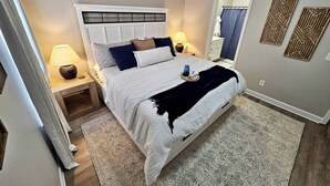 A bedroom with a large bed, two bedside tables with lamps, a headboard, and patterned rugs.