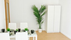 Ein Essbereich mit einem weißen Tisch, gedeckt für vier Personen, weißen Stühlen, einer Zimmerpflanze und einem weißen Kleiderschrank.