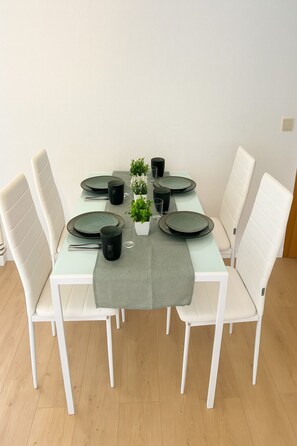 A dining table set with plates, bowls, and glasses, surrounded by white chairs in a room with wooden flooring. - Stylish apartment Stadtfeld-Ost (Magdeburg)
