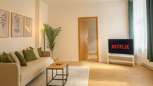 Ein modernes Wohnzimmer mit einer Couch, einem Couchtisch und einem Fernseher, der 'NETFLIX' anzeigt.
