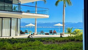A modern hotel with a pool area, palm trees, and a view of the sea and mountains.