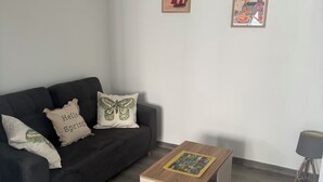 Un soggiorno moderno con un divano nero, un tavolino in legno e due poster appesi alle pareti.