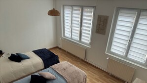 Camera da letto con due letti, una lampada a sospensione e ampie finestre dotate di persiane.