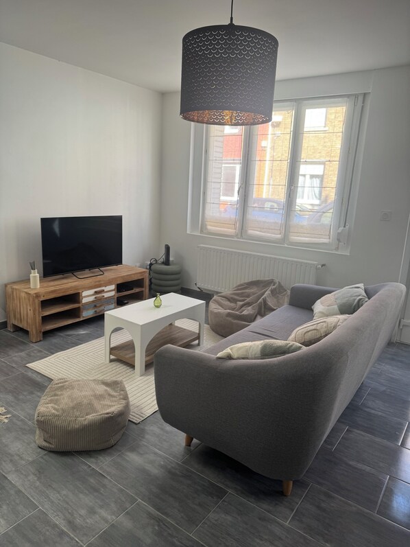 A modern living room with a grey sofa, a white coffee table, and a television on a wooden stand.