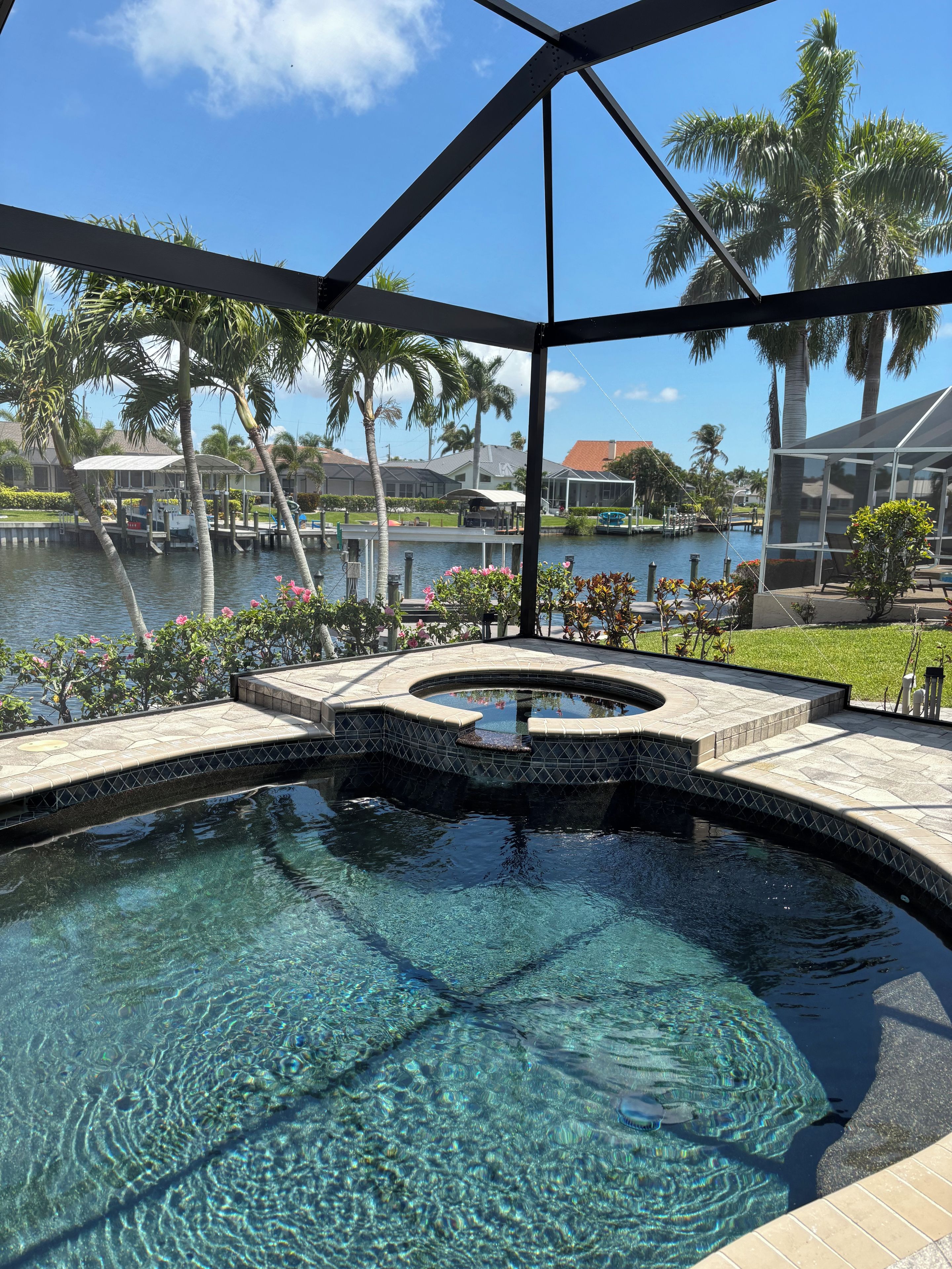 Une piscine aux eaux cristallines, à bords incurvés, entourée d’une terrasse offrant une vue sur un plan d’eau et des palmiers.