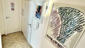 Un corridoio con pavimento in terrazzo, una porta con il cartello ‘no smoking’ e un poster appeso al muro.