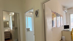 Un corridoio con pavimento piastrellato, una porta che dà su un bagno e una parete con un quadro incorniciato.