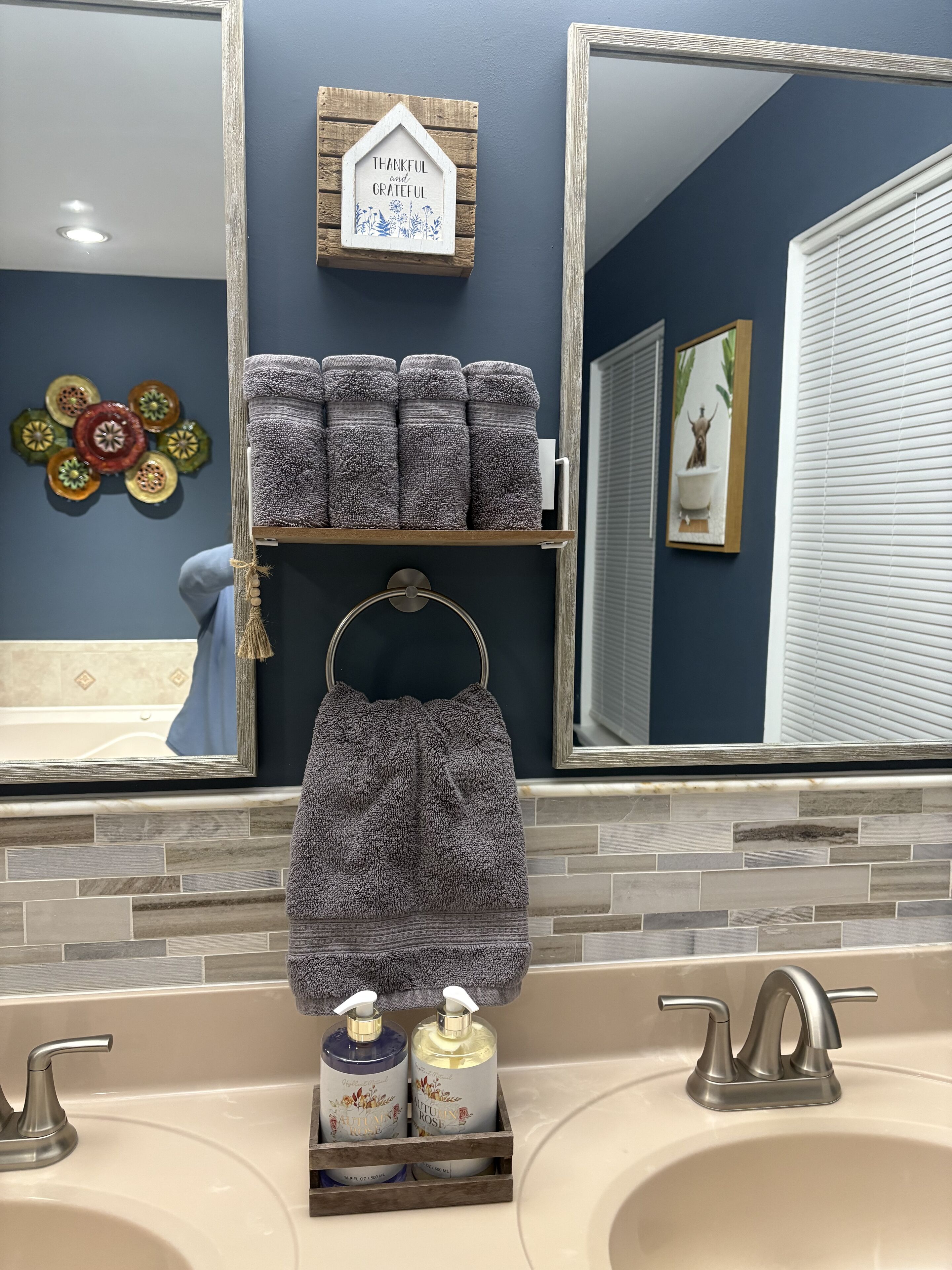 Une salle de bain avec un grand miroir, un porte-serviettes et une étagère où sont pliés des serviettes. On trouve deux flacons de produits de toilette sur le lavabo.