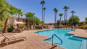 A swimming pool with lounge chairs and palm trees, surrounded by buildings. - Modern Condo Near Stadiums & Westgate Fun (Phoenix)