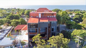 Un immeuble à plusieurs étages, doté d’un toit rouge, de grandes fenêtres et d’une enseigne sur laquelle on peut lire « Hôtel de la Playa ».