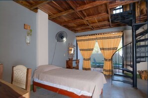 A bedroom with a wooden ceiling, a bed, a chair, a table, a fan, and a staircase. - Madre Tierra Hotel (San Pedro Mixtepec)