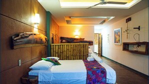 Une chambre d’hôtel moderne avec un grand lit, un ventilateur de plafond, une tête de lit en bois et une étagère murale avec une lampe.