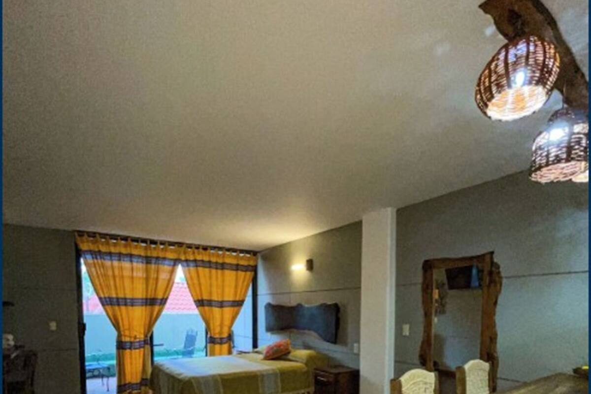Une pièce comprenant un lit, un bureau et une chaise. Il y a une fenêtre avec des rideaux, un miroir au mur et un luminaire au plafond.