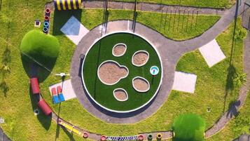 An aerial view of a roundabout with green landscaping, traffic lights, and a central island with multiple circular patches.