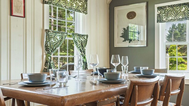 A dining area with a wooden table set for six, surrounded by chairs.