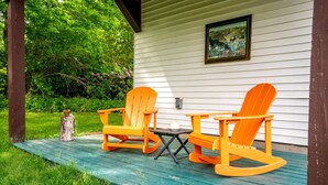 A porch with two rocking chairs and a small table, surrounded by greenery.