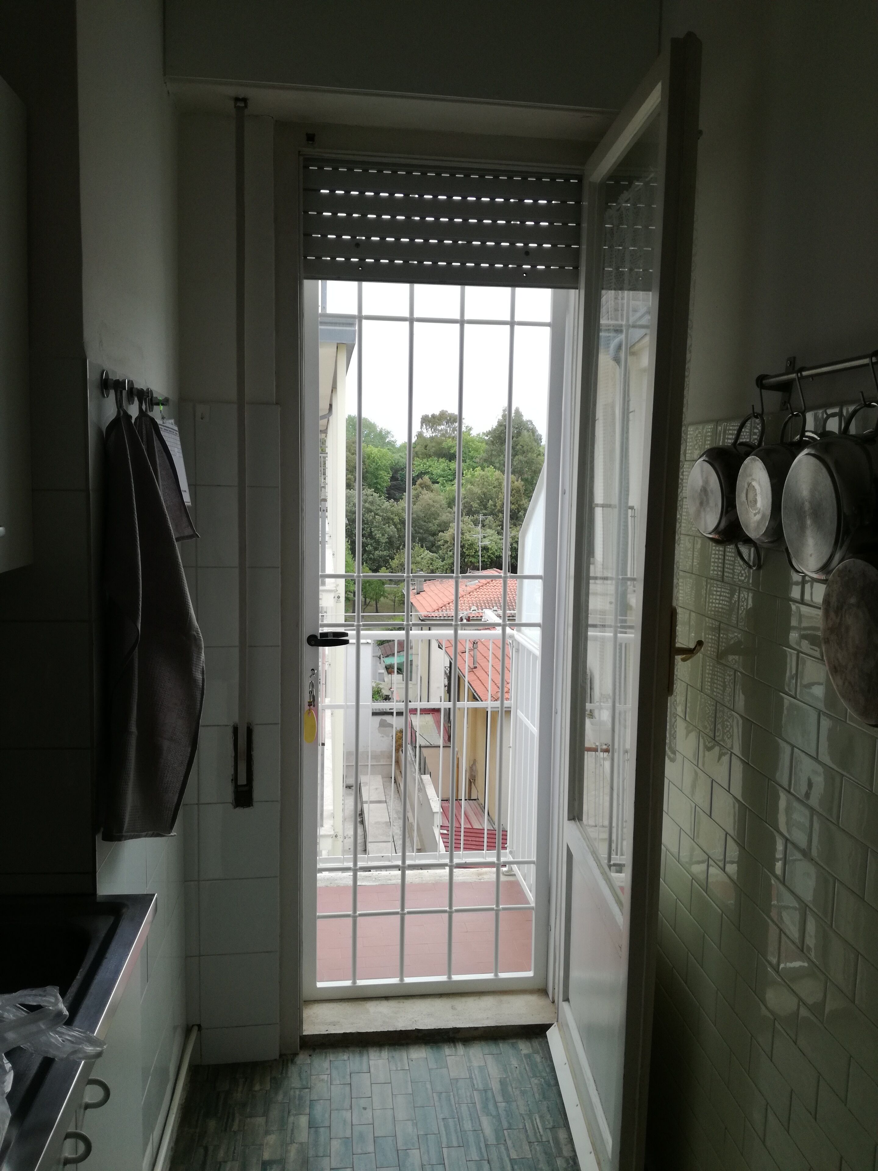 A narrow kitchen with a view through a barred door to a red-roofed building.