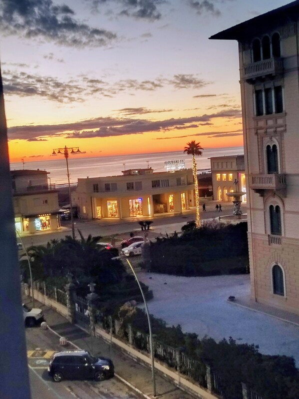 Vista costera con atardecer, edificios con ventanas iluminadas y una palmera.