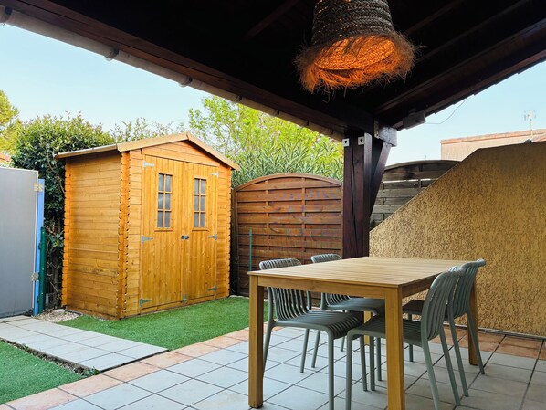A wooden shed, a covered patio with a table and chairs, and a hanging light fixture.